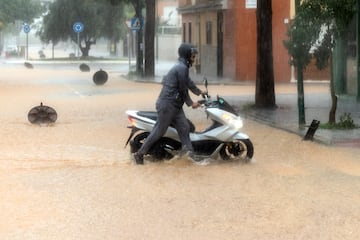 Incidencias en la capital malagueña con motivo de las precipitaciones. Una persona traslada a pie una motocicleta en el barrio de Campanillas, Málaga.