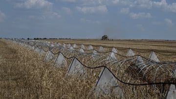 A farmer operates a combine during wheat harvesting near anti-tank fortifications, named 'dragon's teeth' and razor wire near a front line, amid Russia's attack on Ukraine, in the Zaporizhzhia region, Ukraine July 8, 2025. REUTERS/Stringer