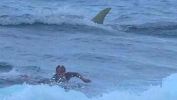 El surfista Rolando Montes remando fuerte para huir de un tiburón del cual asoma la aleta justo detrás suyo en playa Middles (Isabela, Puerto Rico) el 29 de noviembre del 2021.