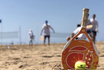 Una pala y una pelota de beach tennis en la playa.