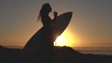 La surfista Luc&iacute;a Marti&ntilde;o con las olas de Lanzarote al fondo tapando una puesta de sol y por tanto a contraluz.