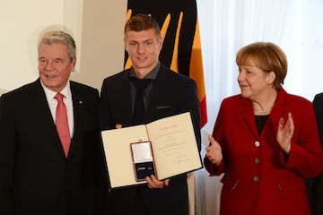 El centrocampista de la selección nacional de fútbol de Alemania, Toni Kroos (centro), posa con el presidente alemán, Joachim Gauck (i), y la canciller alemana, Angela Merkel (d), después de recibir la Hoja de Laurel de Plata, el máximo galardón alemán al éxito deportivo, en el Palacio Presidencial Schloss Bellevue el 10 de noviembre de 2014 en Berlín.