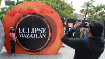 A man takes photos of his daughter in front of a poster in the downtown of Mazatlan, one day ahead of a total solar eclipse in Mazatlan, Mexico April 7, 2024. REUTERS/Henry Romero