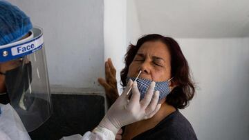 A municipal health worker takes a COVID-19 PCR test sample from a woman at the lobby of a residential building in Caracas, on January 22, 2022. (Photo by Cristian Hernandez / AFP)