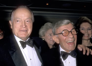 Bob Hope, a la izquierda de la imagen, vivió 100 años llenos de risas y espectáculos. Nacido en 1903 en Londres y criado en Estados Unidos, se convirtió en uno de los cómicos más populares del siglo XX. Brilló en cine, radio y televisión, y fue célebre por sus giras de entretenimiento para las tropas estadounidenses durante décadas. Su humor rápido y su carisma lo hicieron un ícono cultural. Falleció en 2003, justo dos meses después de cumplir el siglo de vida.

George Burns, nacido en 1896, también alcanzó los 100 años con puro estilo. Comenzó en el vodevil y triunfó junto a Gracie Allen en radio y televisión. Su carrera resurgió en los años 70 con 'Oh, God!' y se mantuvo activo hasta el final, con su característico puro y humor seco. Falleció en 1996, dejando un legado de longevidad, ingenio y elegancia cómica que sigue inspirando generaciones.