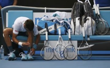 Novak Djokovic cambia sus zapatillas junto a la colección de raquetas que le acompañan cada partido.