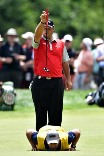 El golfista Patrick Reed sujeta el palo mientras su caddie, tumbado, parece analizar algo del campo. La mirada de Reed parece que quiere decir: ¿si lo dejo caer?