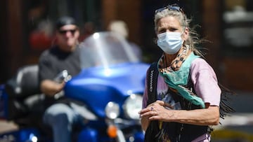 DEADWOOD, SD - AUGUST 08: A woman crosses the street wearing a mask as motorcyclists ride through downtown Deadwood, South Dakota during the 80th Annual Sturgis Motorcycle Rally on August 8, 2020. While the rally usually attracts around 500,000 people, of