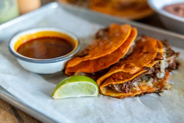 Los tacos de quesabirria son descendientes de la birria, un guiso tradicional popular en Jalisco, México. Trozos de carne de cabra se cuecen a fuego lento durante horas en un caldo con infusión de chile, llamado consomé de birria.