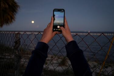 Una mujer usa su teléfono para tomar fotos de la luna tras el lanzamiento del cohete lunar de última generación, el Sistema de Lanzamiento Espacial (SLS) y la cápsula tripulada Orión, parte de la misión de sobrevuelo lunar Artemis II de la NASA.