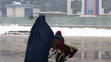 Una mujer con burka lleva a su hijo en una carretilla en Afganistán.