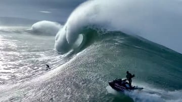 Lucas 'Chumbo' Chianca surfeando una ola gigante en Nazaré, visto desde el lateral, con un jet ski de Red Bull persiguiéndole para el rescate.