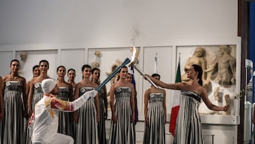 Ancient Olympia (Greece), 26/11/2025.- A handout photo made available by Presidency of the Hellenic Republic shows Greek actress Mary Mina (R), playing the role of High Priestess, passing the flame to the first torchbearer Petros Gaidatzis (L) during the Olympic flame lighting ceremony for the Milano Cortina 2026 Winter Olympics at the Archaeological Museum of Olympia, in southern Greece, 26 November 2025. The Milano Cortina 2026 Winter Olympics will be held from 06 February to 22 February 2026. (Grecia) EFE/EPA/THODORIS MANOLOPOULOS HANDOUT HANDOUT EDITORIAL USE ONLY/NO SALES