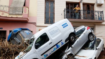 A woman looks from a balcony at piled up cars on a mud-covered street in the aftermath of torrential rains that caused flooding, in Paiporta, Spain, October 31, 2024. REUTERS/Eva Manez