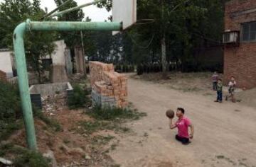 Qin Xulei se prepara para disparar una pelota de baloncesto en un aro en el exterior de su casa en Yichuan condado, Luoyang, provincia de Henan. Qin, de 13 años, se encuentra entre los diez mejores alumnos de su escuela, perdió sus piernas en un accidente de coche cuando tenía tres años. Qin espera representar a China como parte de su equipo nacional de baloncesto de silla de ruedas en los Juegos Paralímpicos en el futuro.