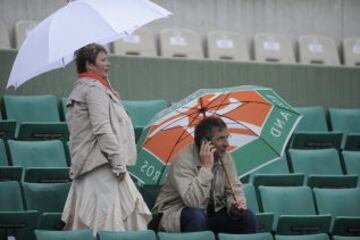 Dos espectadores se protegen de la lluvia bajo los paraguas después de que los partidos del torneo de Roland Garros hayan sido aplazados por la lluvia.