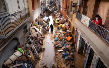 La gente camina por una calle con muebles amontonados y basura a los lados en una zona afectada por las inundaciones en Paiporta, Valencia.