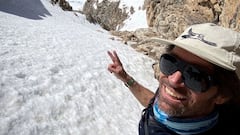 El snowboarder Jeremy Jones sonriendo, con gafas de sol y manga corta y haciendo el se&ntilde;al de la victoria, justo antes de bajar por una canal llena de nieve en la monta&ntilde;a. 
