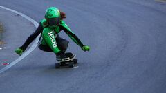 La alicantina Cristina Verdú practicando longboard downhill con un traje y casco verde en una curva, seguida de otra rider.