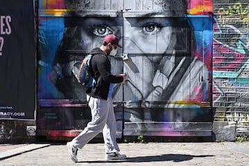 A man wearing a protective face mask walks past a piece of grafitti of artist BK Foxx wearing her grafitti mask created by French street artist Zabou in East London on April 19, 2020, during the novel coronavirus COVID-19 pandemic. 