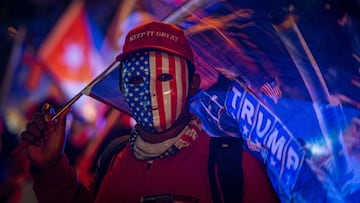 Un simpatizante de Donald Trump viste careta con la bandera estadounidense y una gorra que dice "Mantén (América) grandiosa" mientras espera los resultados de las elecciones presidenciales hoy, en el icónico café Versailles de la Calle Ocho en Miami, Florida.