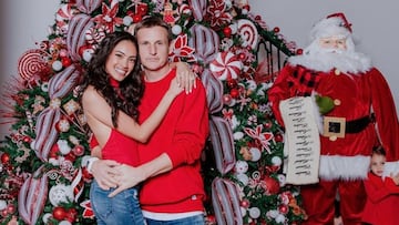 El empresario del skate Rob Dyrdek abrazado junto a su pareja frente a un árbol de Navidad grande, con un muñeco de Papá Noel y su hijo escondido en los brazos del muñeco.