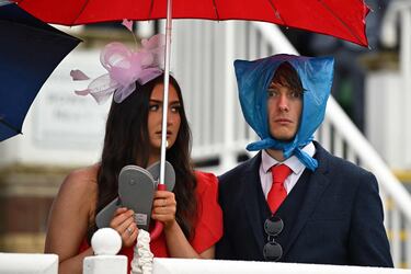 La lluvia hizo acto de presencia en el hipódromo de Aintree, en Liverpool, durante el segundo día de carreras del Grand National. En la imagen, una mujer se protege del agua bajo un paraguas mientras sostiene unas chanclas en la mano, al tiempo que su acompañante mira a la cámara sorprendido con una bolsa de plástico en la cabeza. 