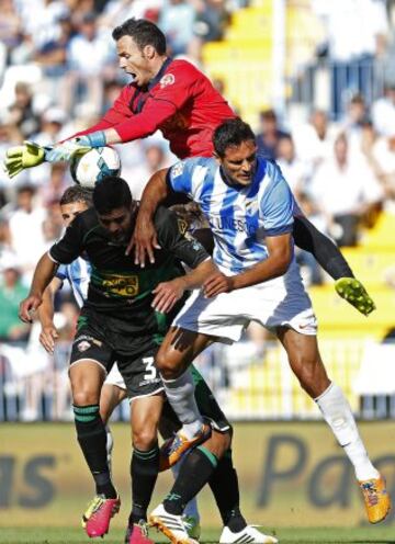 El portero del Elche, Manu Herrera, salta por el balón ante su compañero el defensa Alberto Tomás Botía (i) y el delantero paraguayo del Málaga Roque Santa Cruz (d), durante el partido de la jornada 36, de la Liga de Primera División de Fútbol, esta tarde en el estadio de La Rosaleda.