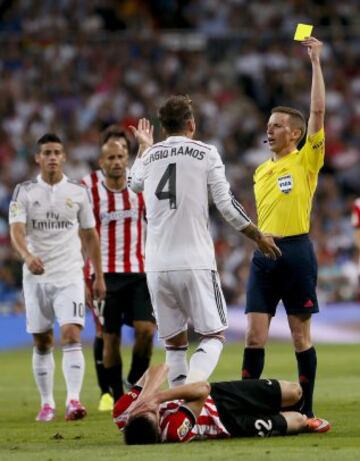 El árbitro Hernández Hernández muestra tarjeta amarilla a Sergio Ramos tras una entrada sobre el delantero vasco Guillermo.