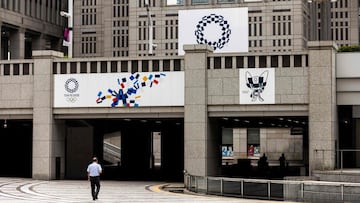 Un hombre camina por la calle delante del logo de los Juegos Ol&iacute;mpicos de Tokio 2020.