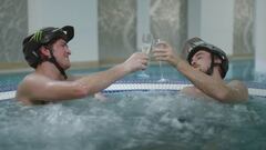 Los pilotos de MTB Brendan Fairclough y Olly Wilkins en un jacuzzi, brindando con cava y sonriendo, con el casco de mountain bike A3 de Troy Lee Designs puesto. 