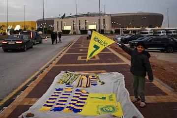 Un niño sostiene una bandera con el nombre de Ronaldo mientras vende souvenirs frente al estadio Mrsool Park donde se está presentando al futbolista portugués Cristiano Ronaldo, en Riad, Arabia Saudí,