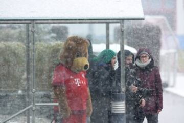 Baerli, la mascota del Bayern de Munich, y varios periodistas durante la sesión de entrenamiento del equipo se resguardan de la fuerte nevada.