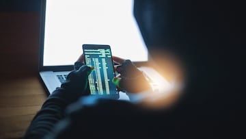 Shot of an unrecognisable hacker using a cellphone and laptop in the dark
