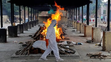 A priest wearing personal protective equipment (PPE) walks in front of the body of a person who died of the coronavirus disease (COVID-19), as he collects woods to make a funeral pyre at a crematorium in New Delhi, India, July 3, 2020. REUTERS/Anushree Fa