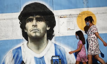 A woman and a girl walk by a mural of Diego Maradona (BA)