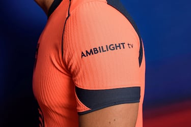 Un llamativo color mango brillante domina en la camiseta –también en los pantalones y las medias– acompañado de varios detalles en azul marino en forma de franjas en el cuello y en la espalda y de filetes que dibujan una forma geométrica en la parte frontal, con el logotipo de Spotify en el centro.