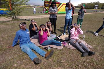 Un grupo de aficionados, con gafas protectoras para ver el eclipse solar, observan el eclipse solar durante el Masters de Augusta.