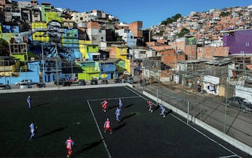 21. Residentes jugando al fútbol en un campo con la imagen del jugador de fútbol brasileño Gabriel Jesús en el fondo, pintado en las paredes de las casas de la favela donde vivió durante su infancia en las afueras de Sao Paulo.