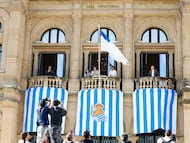 El alcalde de San Sebastián, Jon Insausti (c, i), y el ex jugador de la Real Sociedad, Xabi Prieto (c, d), presentan las banderas blanquiazules colocadas en la fachada del Ayuntamiento donostiarra para animar al equipo de la ciudad en la final de la Copa del Rey contra el Atlético de Madrid que se celebrará en Sevilla el próximo 18 de abril. EFE/Juan Herrero.