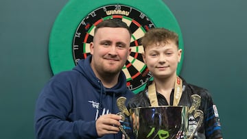 El jugador de dardos inglés Luke Littler posa con el belga Lex Paeshuyse tras entregarle el trofeo de campeón del mundo junior de dardos.