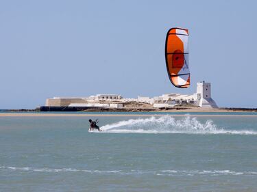 Frente al castillo de Sancti Petri y junto al caño del mismo nombre, esta playa extiende sus arenas movidas por las fuertes corrientes mareales de la zona. Un paisaje cargado de diferentes elementos en el que dunas, marismas, un puerto pesquero y plataformas rocosas cubren el terreno. La playa dividida en dos tramos, concentra la mayoría de los servicios al norte del espigón coincidiendo con la mejor zona para el baño. La zona al sur del espigón es conocida como playa “Punta de Piedras” por su fondo rocoso. Queda definida en su parte posterior, por un talud rojizo en cuya superficie se desarrolla un sistema dunar protegido que conecta con un pinar costero. Se puede acceder a esta playa desde la carretera del Puerto de Sancti Petri. El poblado de Sancti Petri es un lugar tradicional de pescadores dedicados a la pesca del atún rojo mediante el arte de la almadraba. En el poblado existían tanto casas de marineros como fábrica de conservas, hasta el año 1973, cuando se clausuró la práctica de este arte en la zona. Actualmente en el poblado existe un club náutico, asociaciones de pescadores, algunos restaurantes y locales de alquiler de actividades náuticas. 