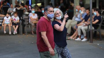 Imagen de dos ciudadanos paseando por las calles de Barcelona y portando mascarillas.