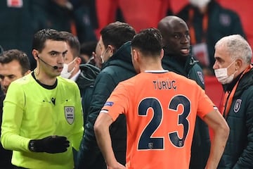 08 December 2020, France, Paris: Romanian referee Ovidiu Hategan (L) talks to Istanbul Basaksehir staff next to Demba Ba (2nd R) during the UEFA Champions League group H soccer match between Paris Saint-Germain and Istanbul Basaksehir at Parc des Princes.