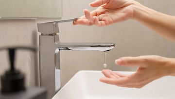 Close up of woman's hand turn on faucet and a drop of water dripping out into hand at white ceramic wash basin in modern design bathroom