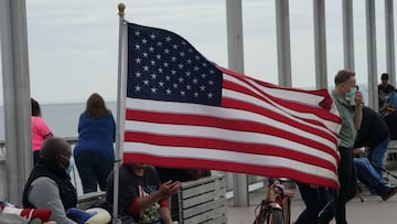 A man wearing a face mask sits near an American flag on a pier at Coney Island amid the coronavirus pandemic on May 24, 2020 in New York. - Parts of New York state that saw fewer virus cases have already begun to ease lockdown restrictions, but they have 