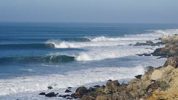 Cinco olas rompiendo en la costa de Marruecos, una tras otra, en la marejada del año, en marzo del 2021. Con algunos surfistas en el agua y las rocas de la costa asomando por la derecha.