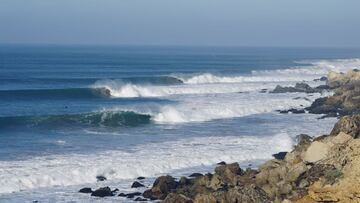 Cinco olas rompiendo en la costa de Marruecos, una tras otra, en la marejada del a&ntilde;o, en marzo del 2021. Con algunos surfistas en el agua y las rocas de la costa asomando por la derecha. 