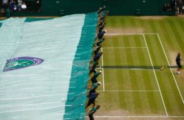 Recogepelotas cubriendo la pista de tenis de Wimbledon ante la lluvia que ha hecho cancelar el partido entre Federer y Djokovic.