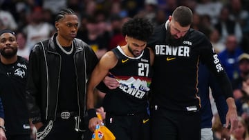 Jamal Murray, base de Denver Nuggets, sale lesionado de la cancha apoyado en sus compañeros Peyton Watson y Jonas Valanciunas.